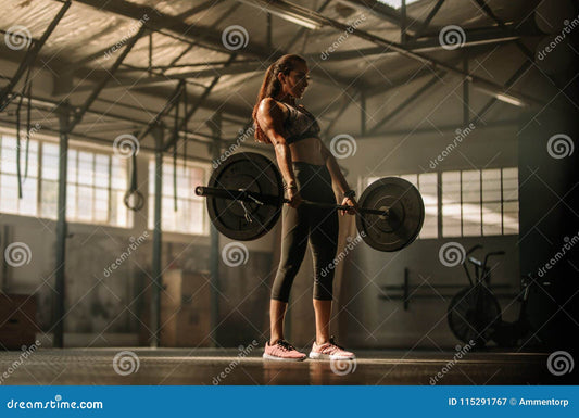 A strong woman is lifting a barbell loaded with weights in a well-lit gym, showcasing her strength and determination.